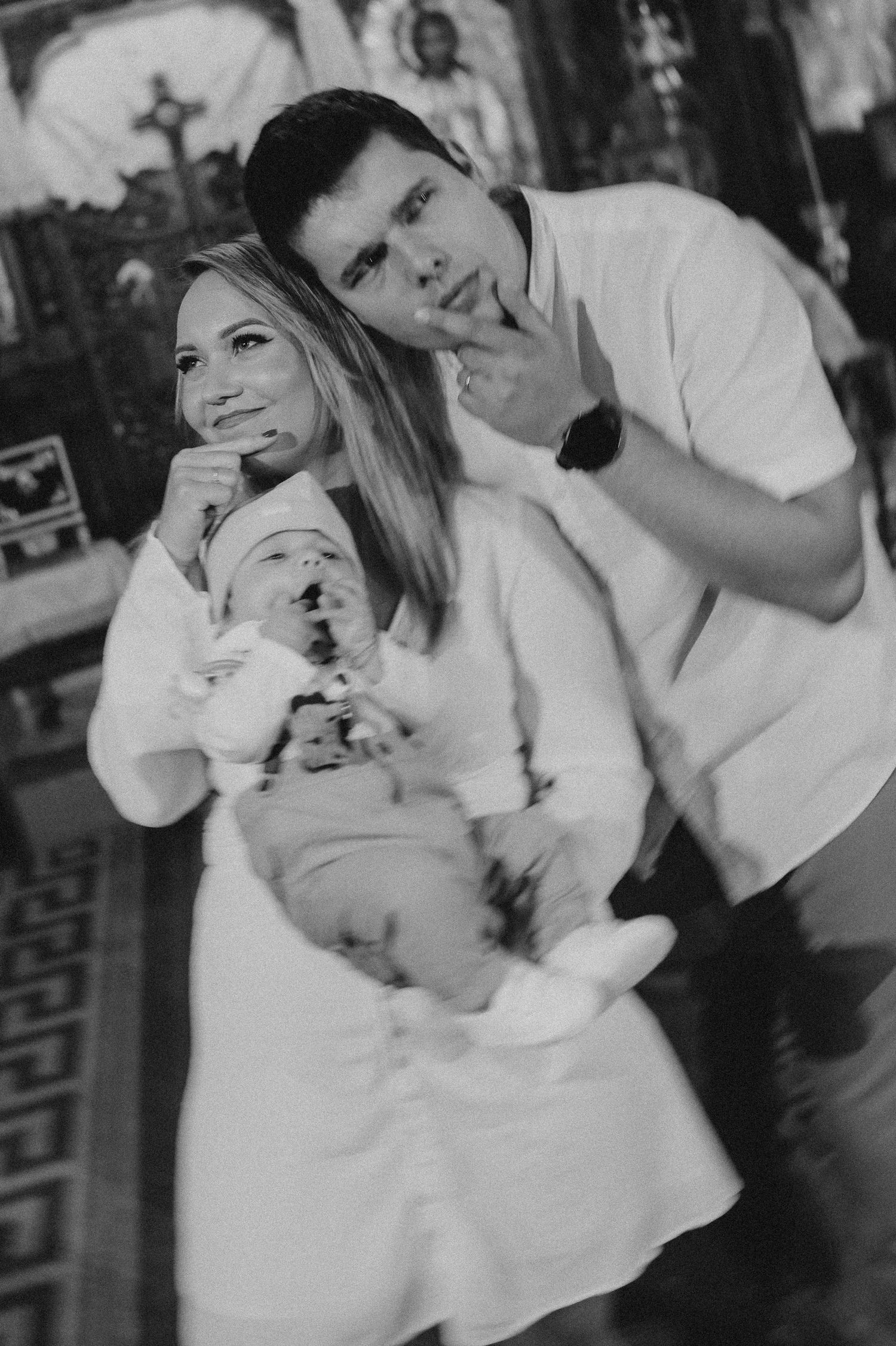 Black and white photo of smiling couple holding newborn baby in a church.