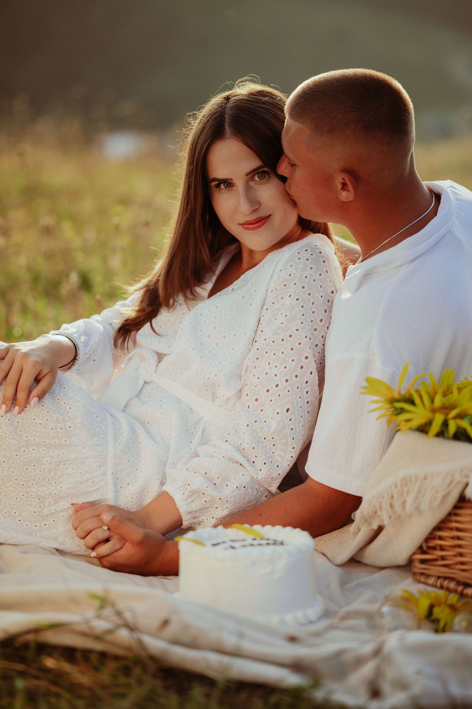 Man kissing woman in white dress cheek during romantic outdoor mountain picnic.