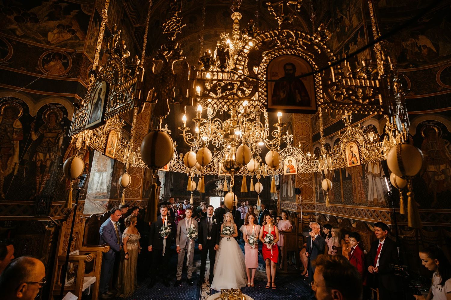 Ornate Orthodox church interior filled with wedding guests under golden chandeliers during a ceremony.