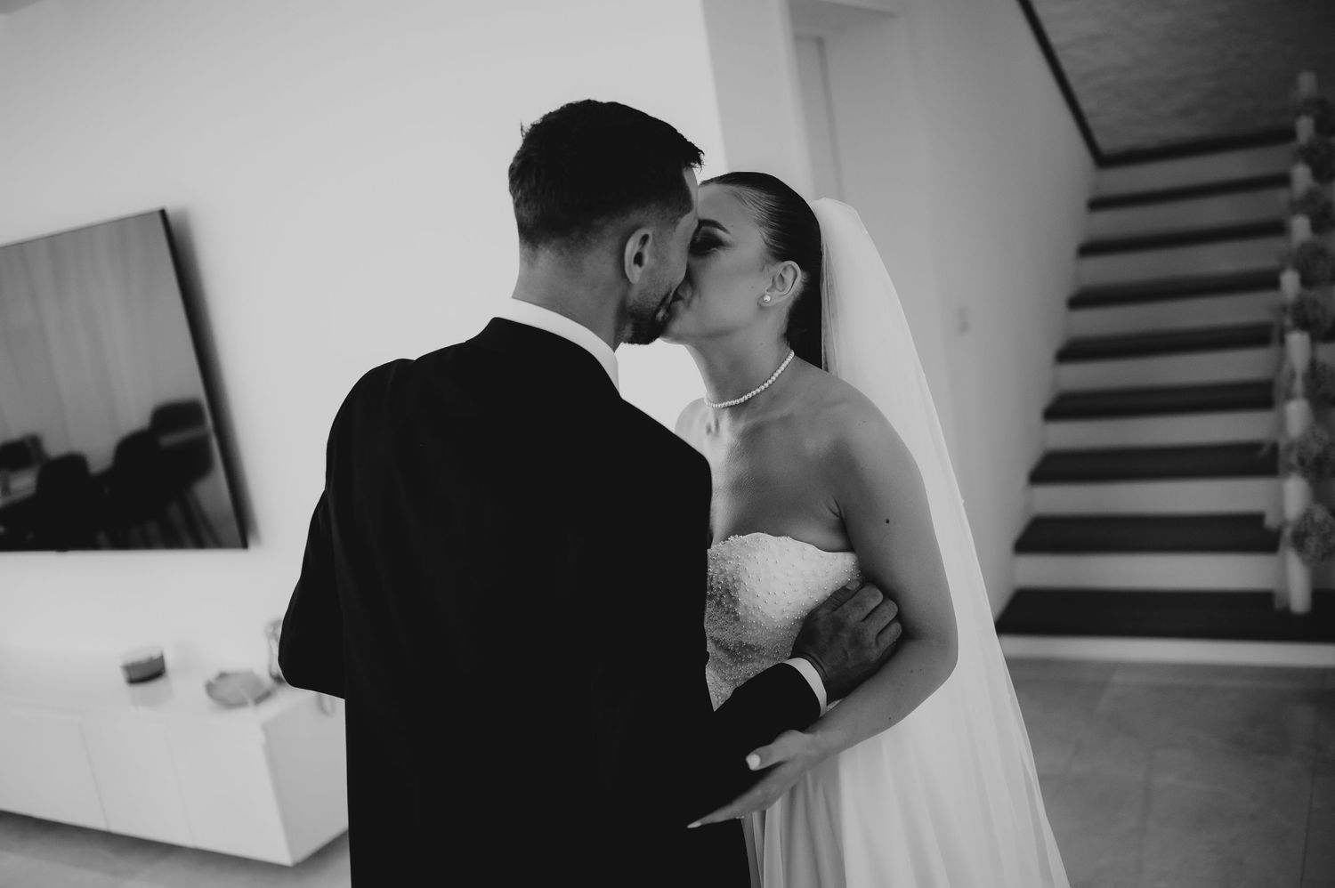 Black and white photo of bride and groom sharing a tender kiss in elegant wedding attire.
