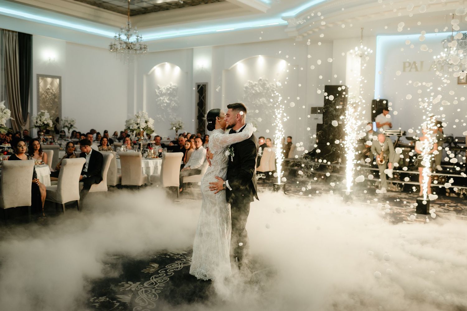 Bride and groom kissing during first dance surrounded by dry ice fog and sparkler fountains.