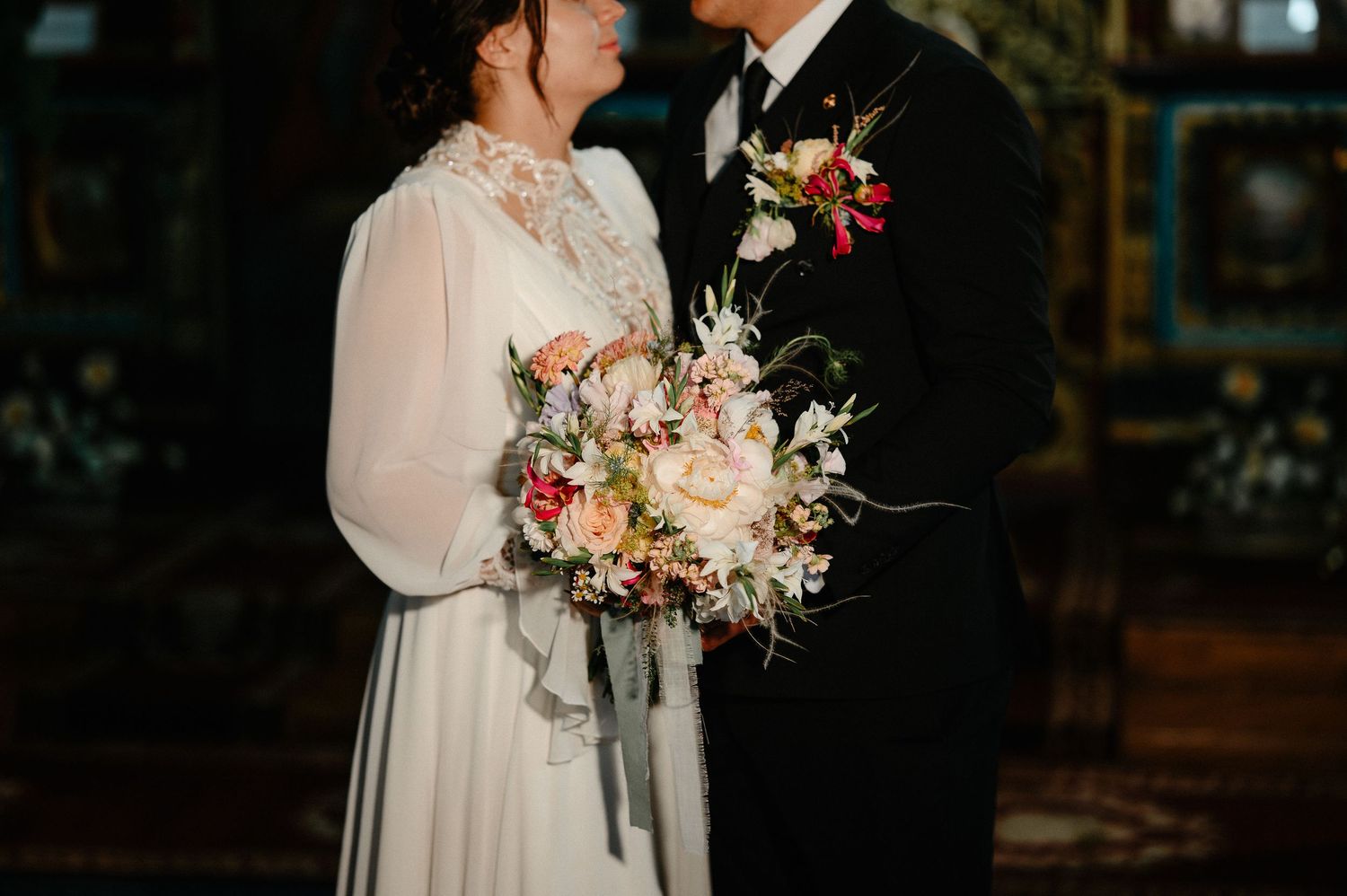 Couple in wedding attire holding beautiful floral bouquet with roses and wildflowers.