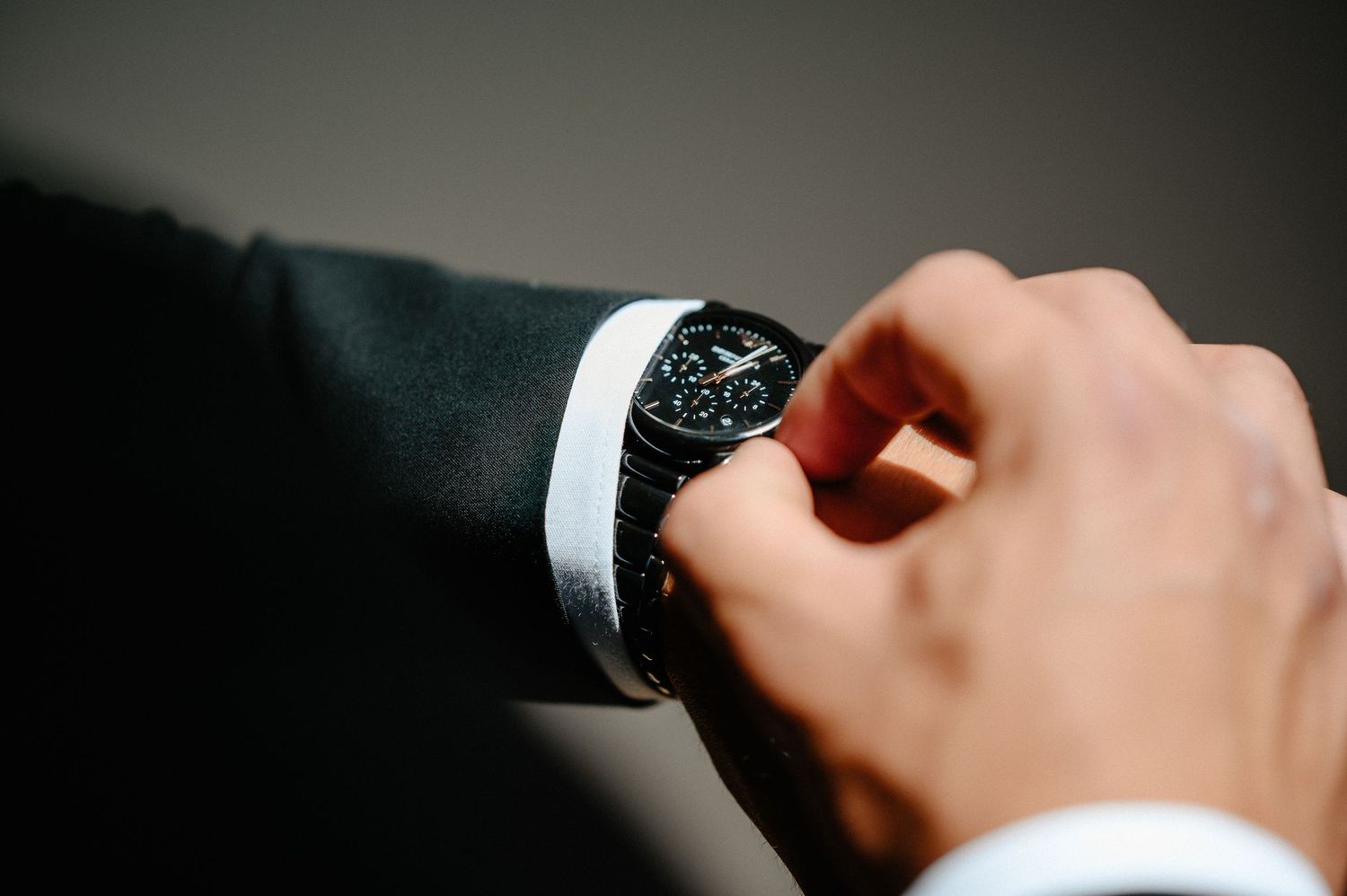 Man in black suit checking time on a black wristwatch, close-up shot of luxury watch on wrist.