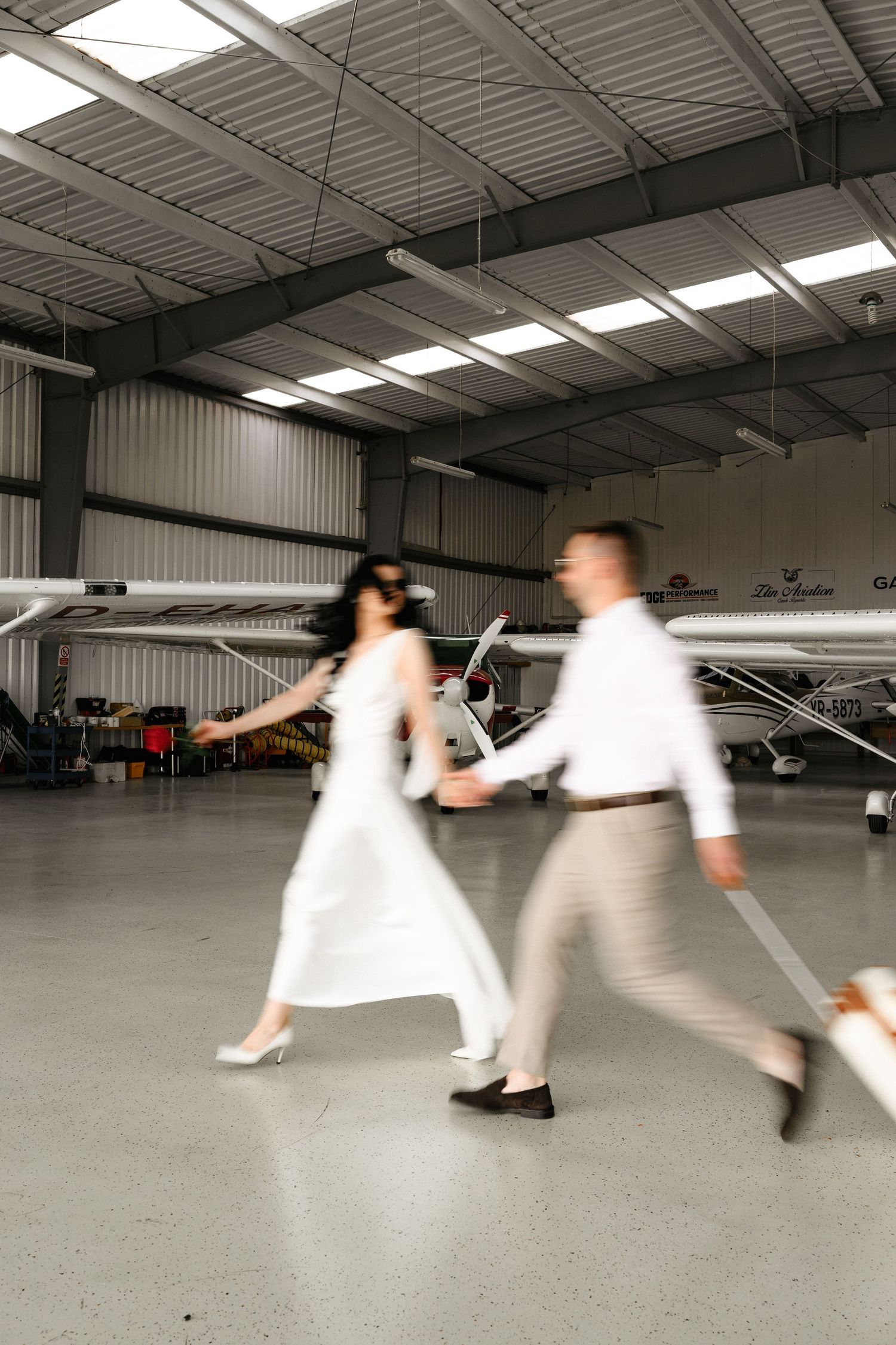 Bride and groom walking hand in hand through an airplane hangar on their wedding day.