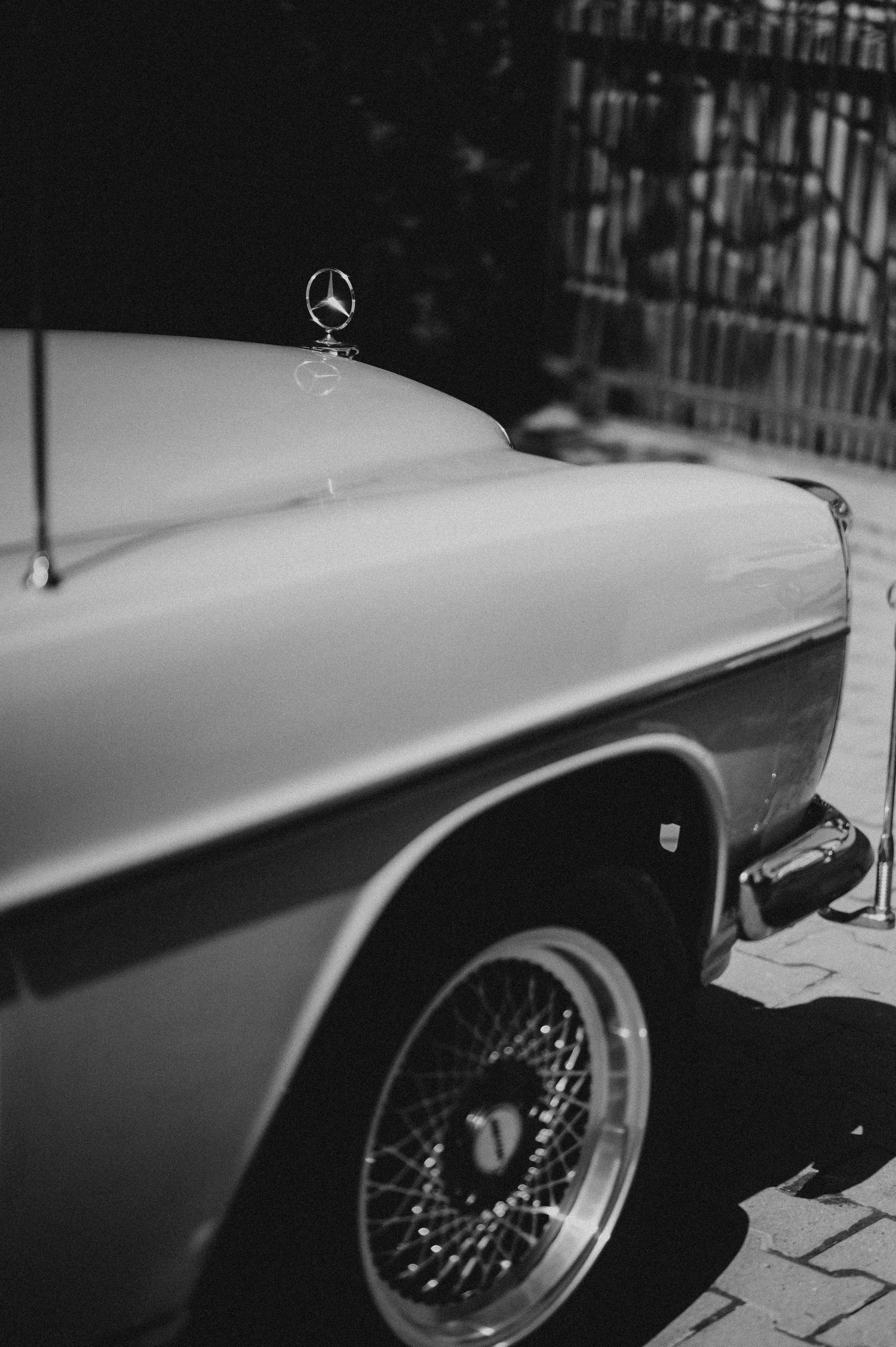 Black and white photo of a classic vintage Mercedes-Benz car with wire spoke wheels and hood ornament.