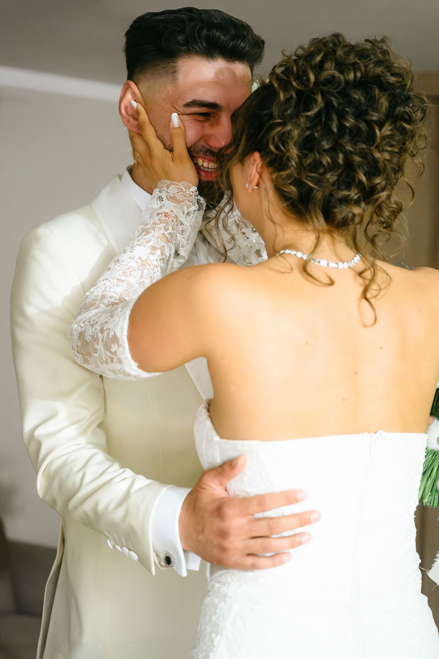 A joyful bride and groom share an intimate moment, embracing in wedding attire, as the bride tenderly touches the groom's smiling face.