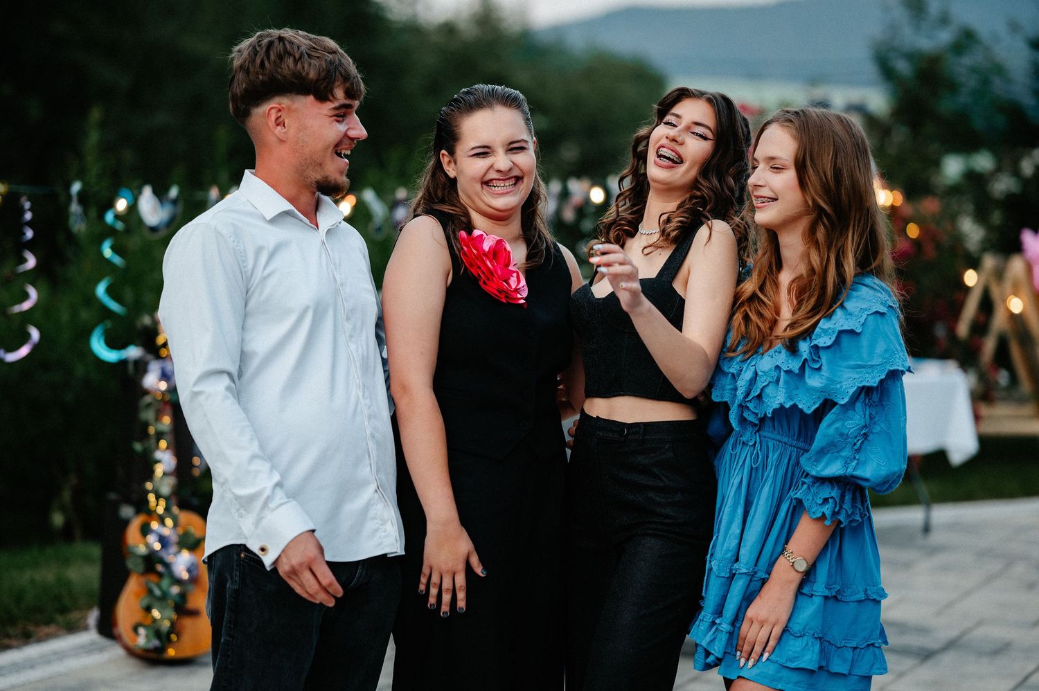 Four young adults laughing and posing together at an outdoor evening party celebration.