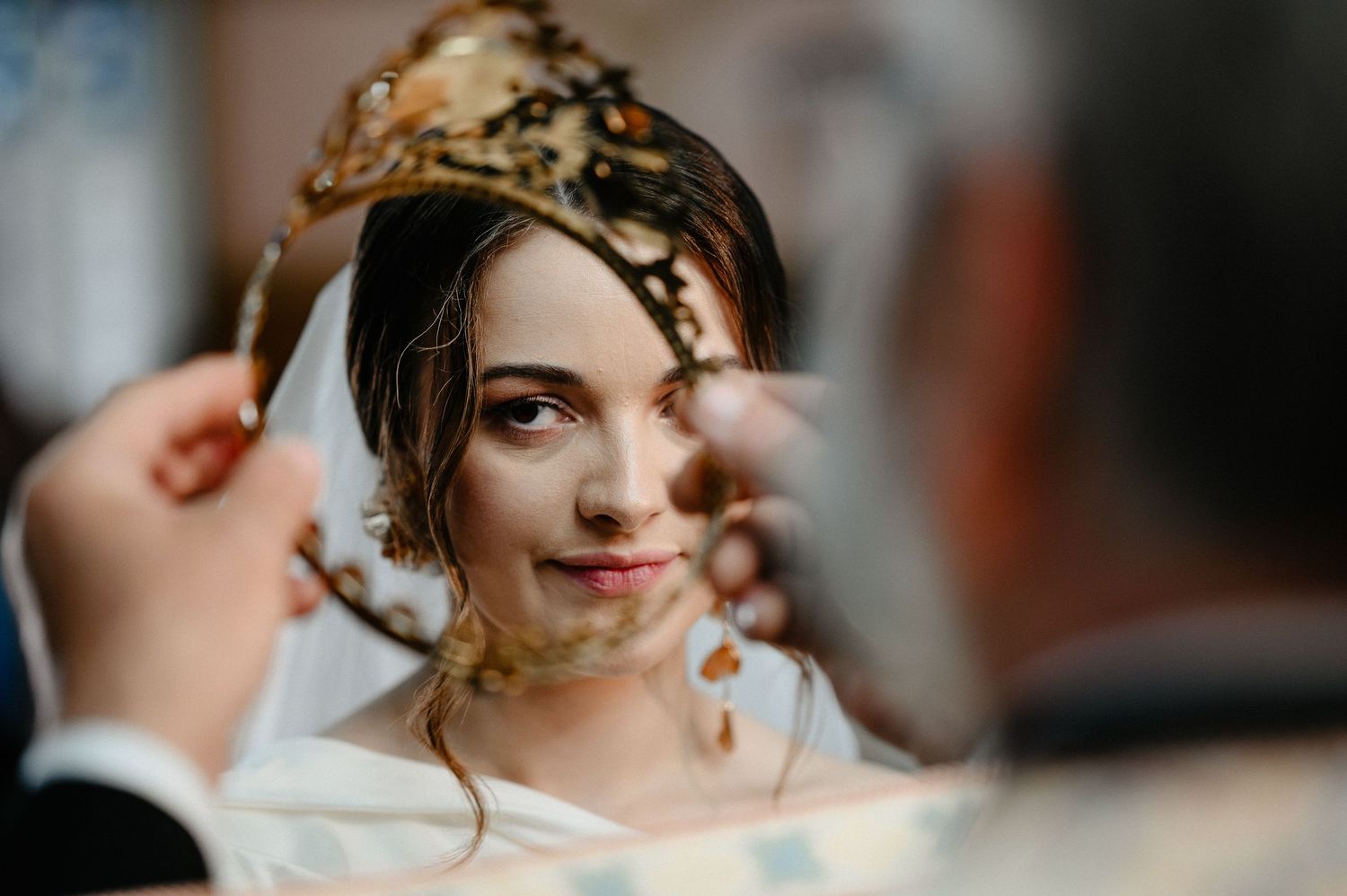 Bride wearing golden crown during Orthodox wedding ceremony with veil and earrings.