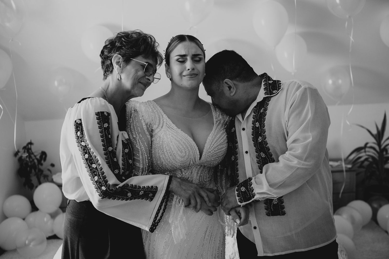 Black and white photo of bride embraced by two guests at wedding.
