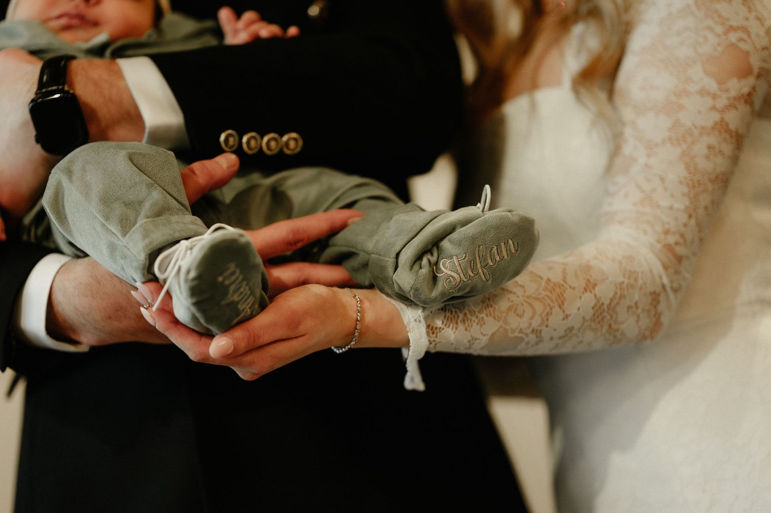 Close-up of a newborn baby in a sage green outfit being held by parents at a christening ceremony.