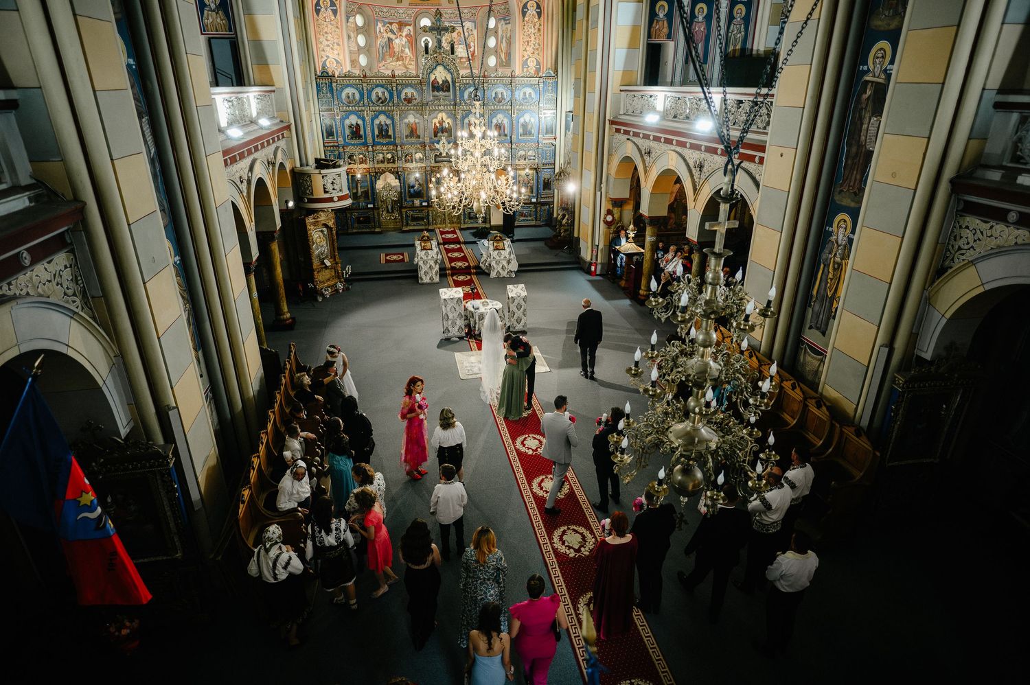 Overhead view of Orthodox church wedding reception with guests mingling under grand chandeliers.