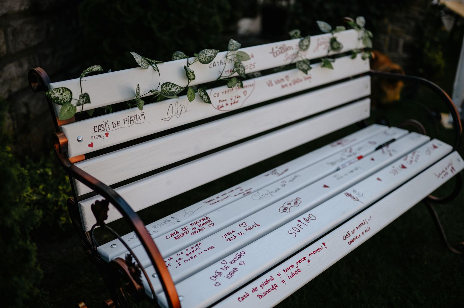 Decorative white wooden wedding guest book bench with handwritten messages and floral designs.