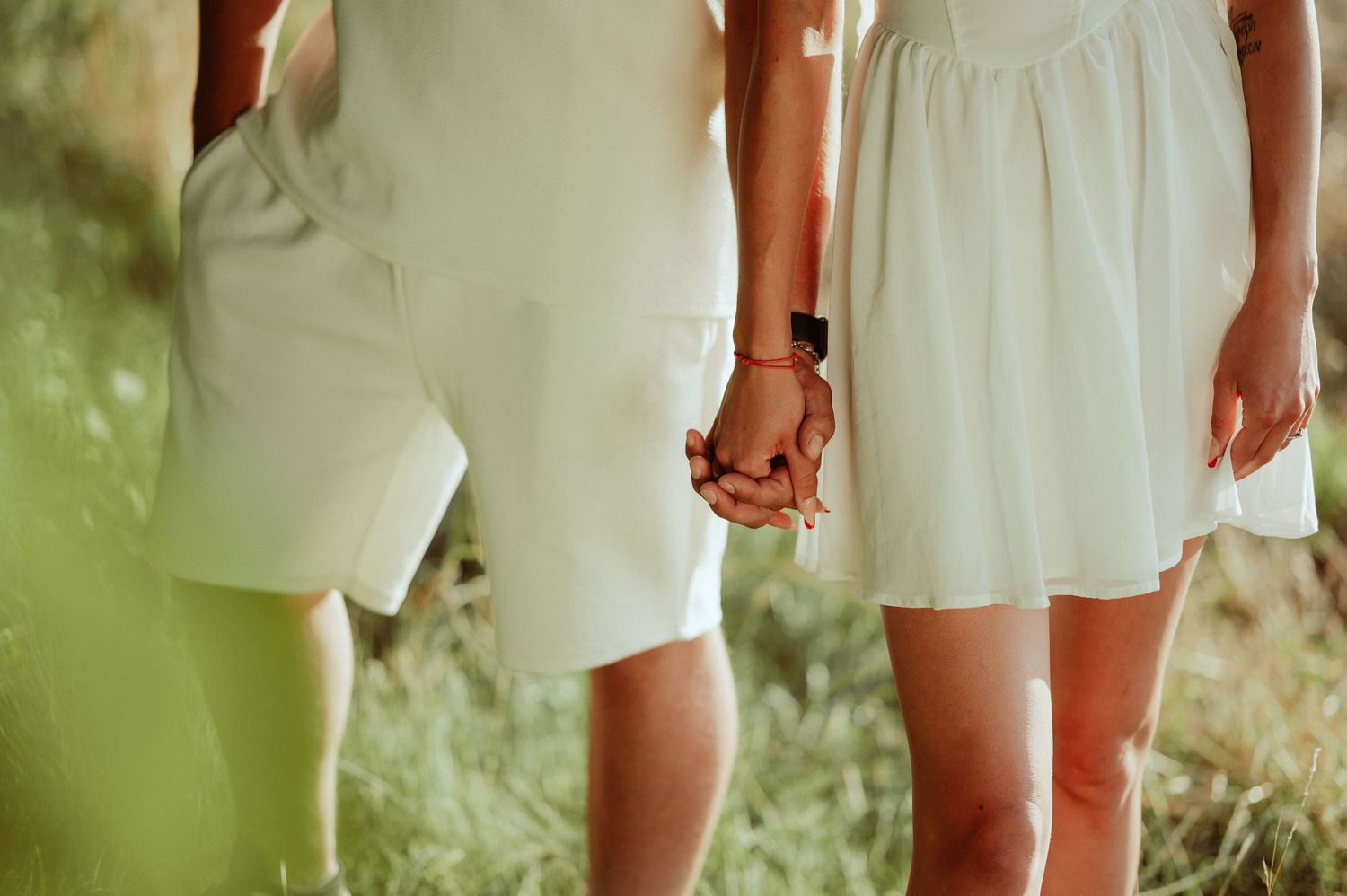 Close-up of couple holding hands wearing white outfits outdoors.