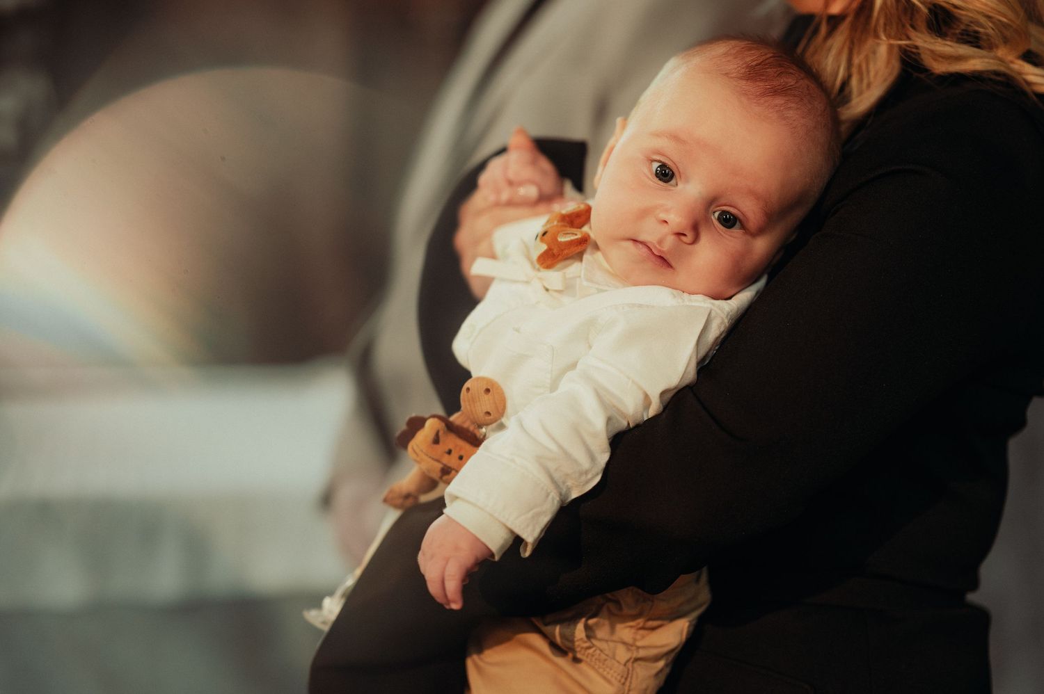 Close-up of a newborn baby in white outfit being held during a christening ceremony.