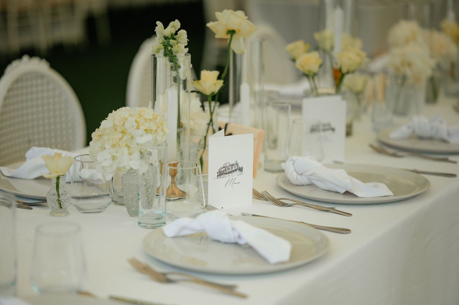 Sophisticated wedding table setting with white flowers, glass bottles, folded napkins, and silver charger plates.