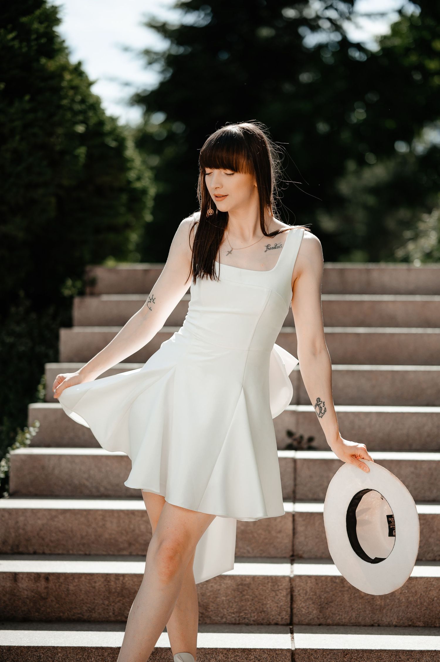 Beautiful woman in white sundress holding a hat while standing on outdoor stone staircase.