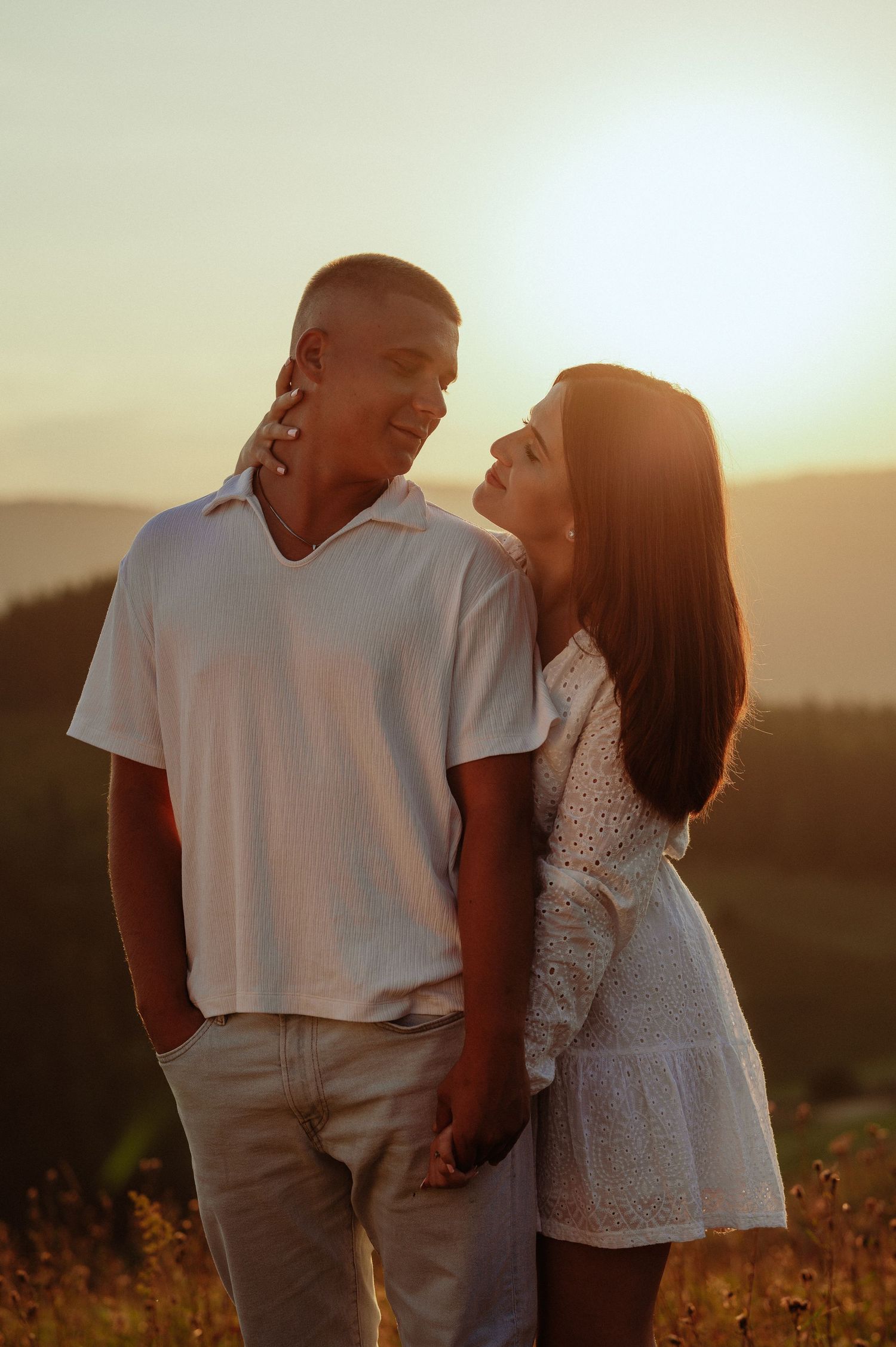 Romantic couple holding hands and gazing at each other during golden sunset in mountains.
