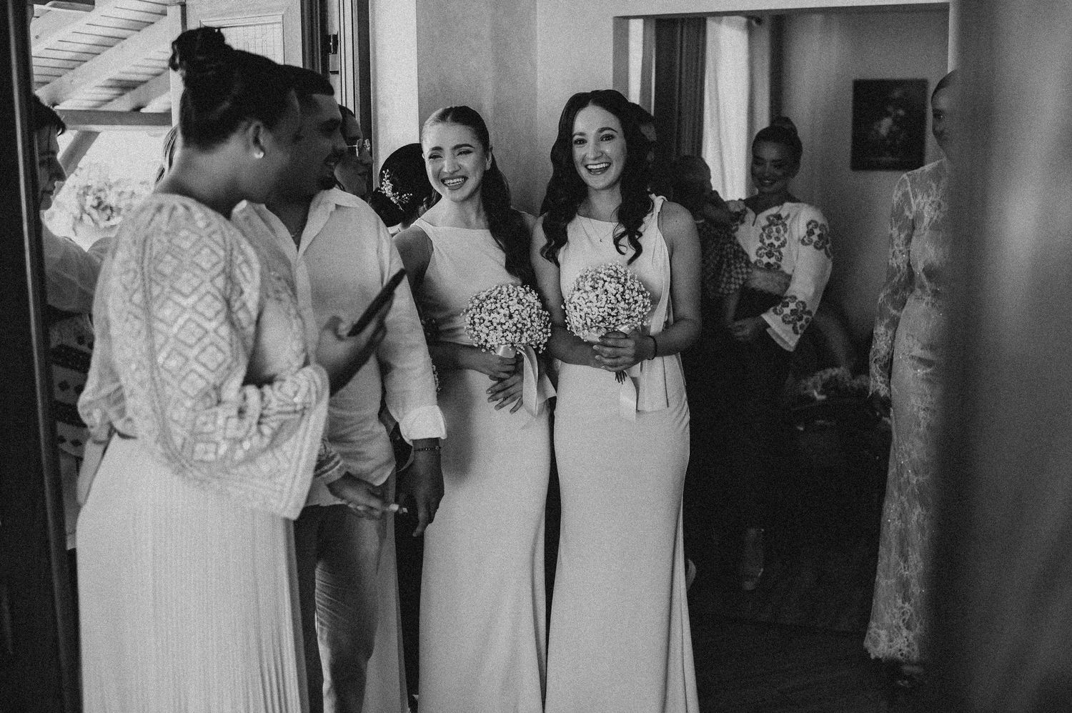 Black and white photo of smiling bridesmaids in white gowns holding floral bouquets.