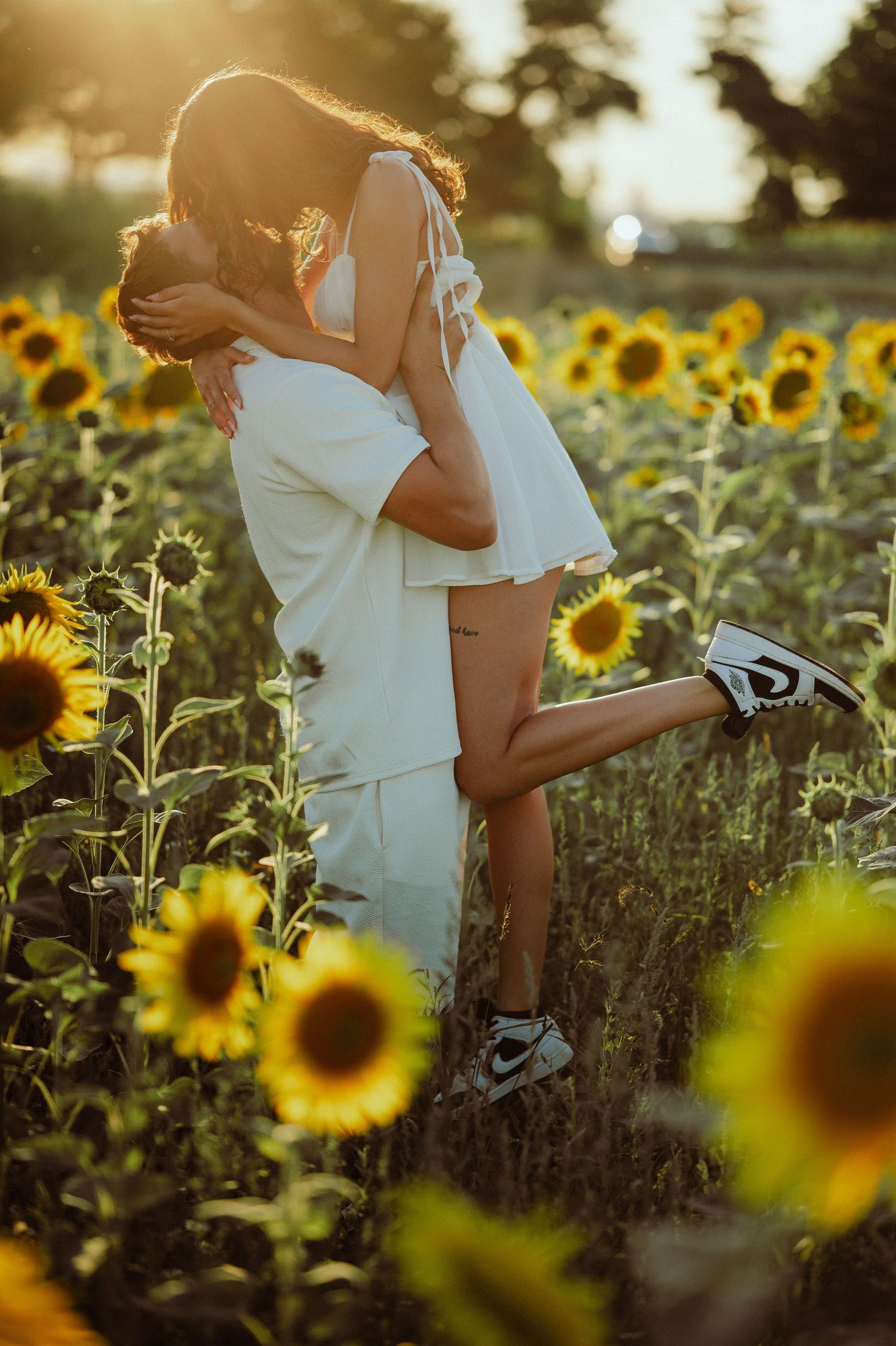 Couple sharing a romantic kiss in a sunflower field bathed in warm golden sunset light.