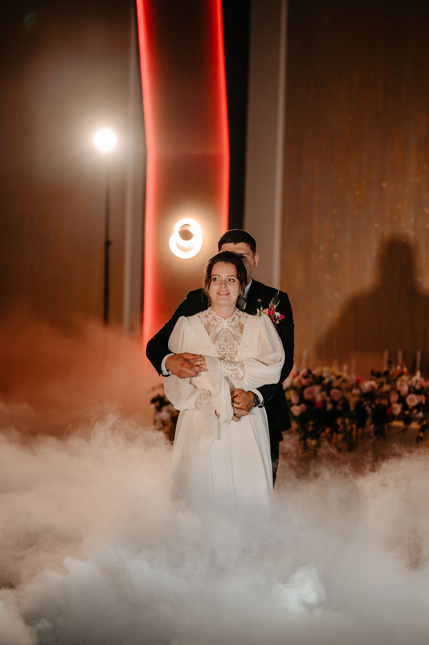 Bride and groom share first dance surrounded by dramatic fog on a warmly lit wedding reception dance floor.