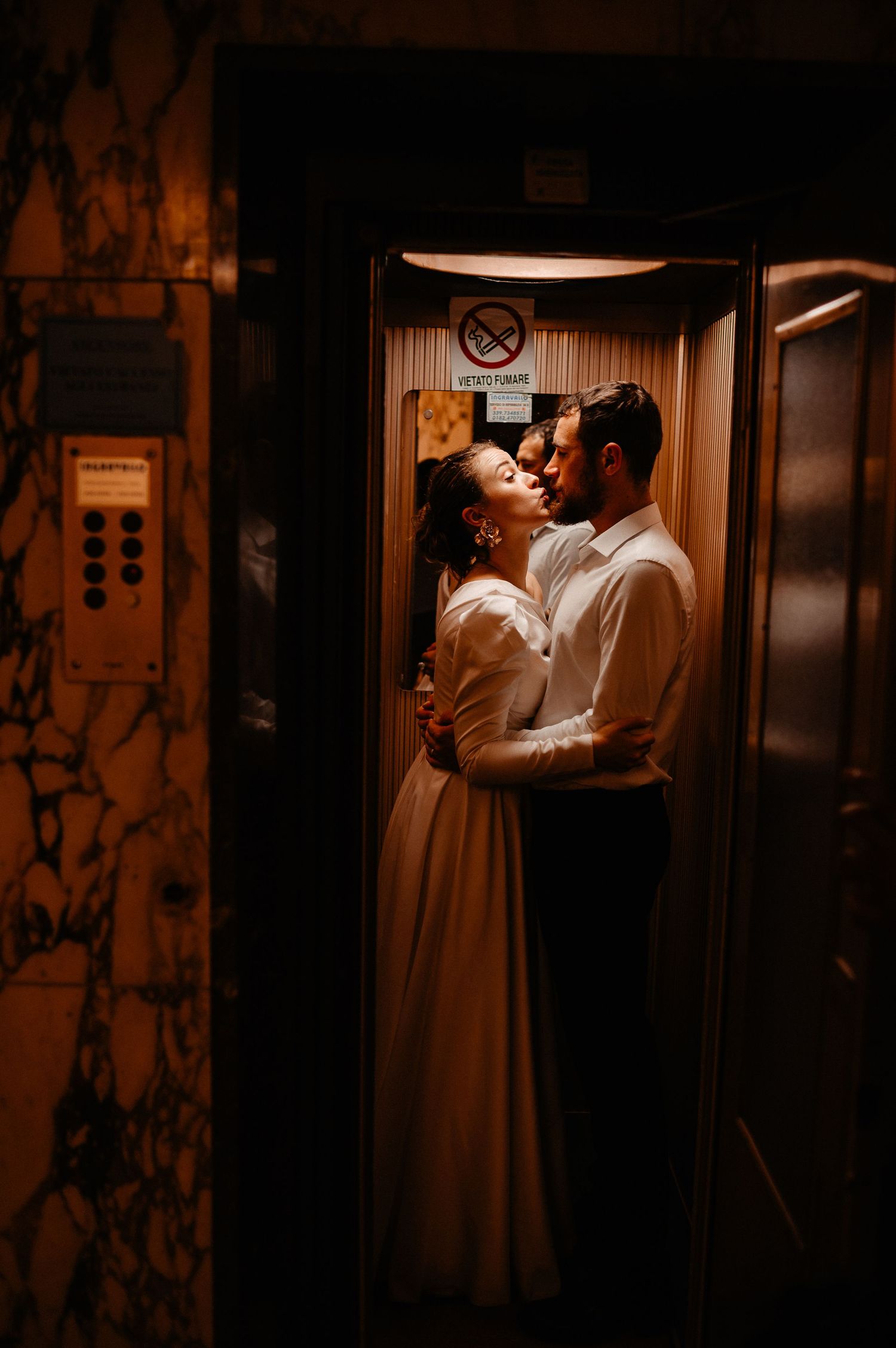 Romantic couple nearly kissing in warmly lit vintage elevator with marble walls.