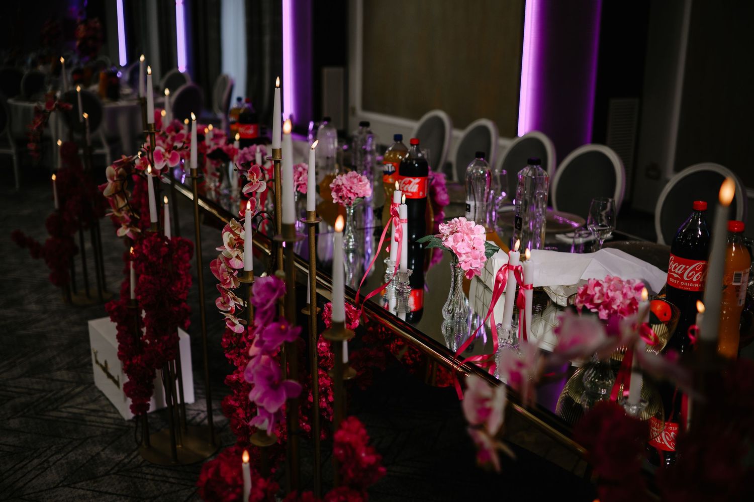 Dimly lit wedding reception table decorated with pink orchids, candles, and floral centerpieces in moody lighting.
