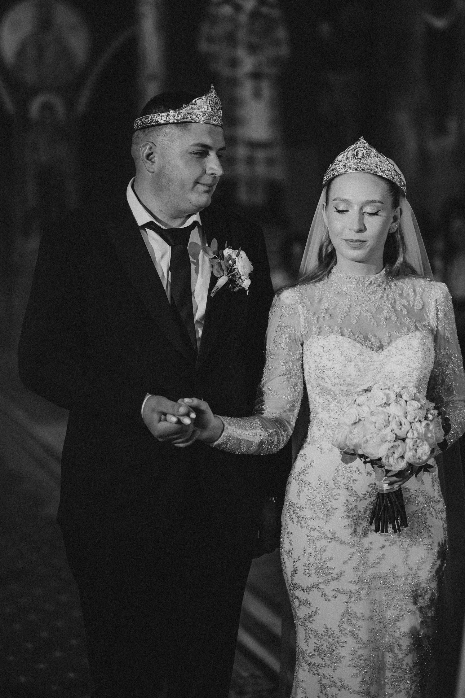 Black and white photo of bride and groom wearing crowns in church.