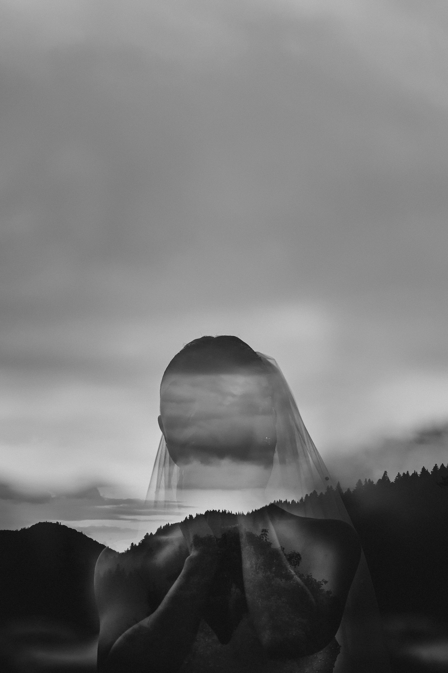 Artistic double exposure black and white portrait of bride with veil merged with misty mountain landscape.