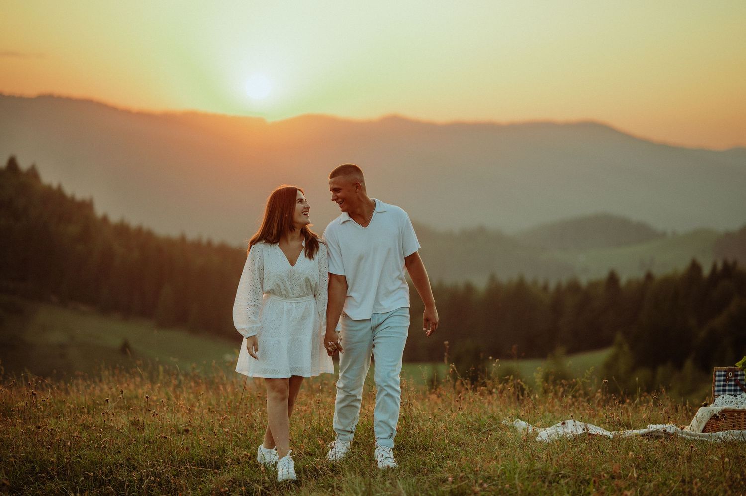 Happy couple holding hands and smiling at each other during vibrant mountain sunset.