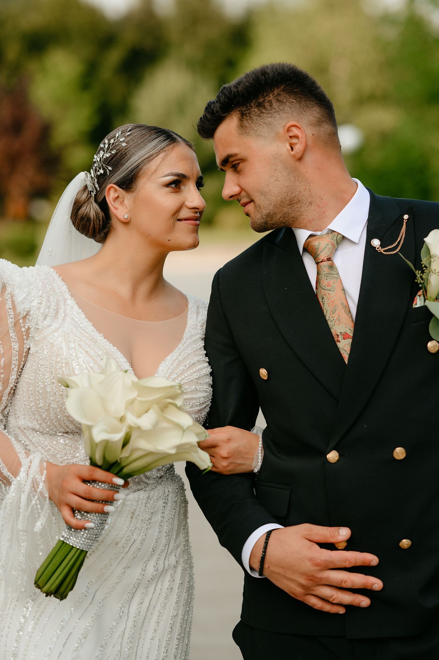 Wedding couple gazing lovingly at each other, bride in sparkly white gown with veil, groom in black suit with floral tie.