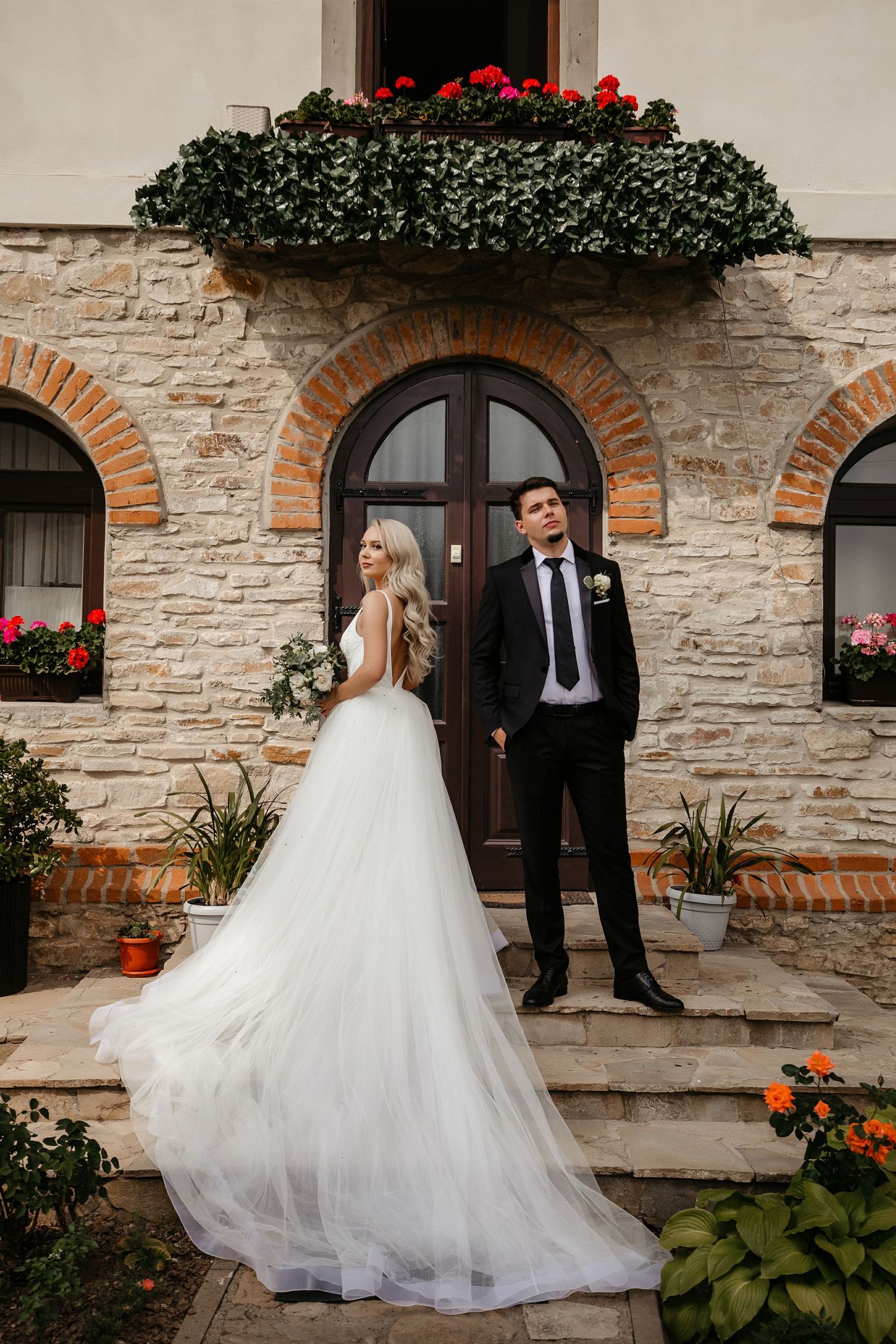 Bride in flowing tulle gown and groom posing outside rustic stone building.