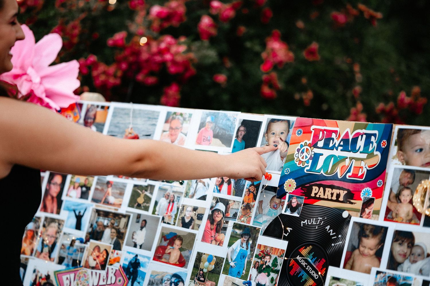Woman pointing at colorful photo collage board with Peace and Love Party theme at outdoor event.