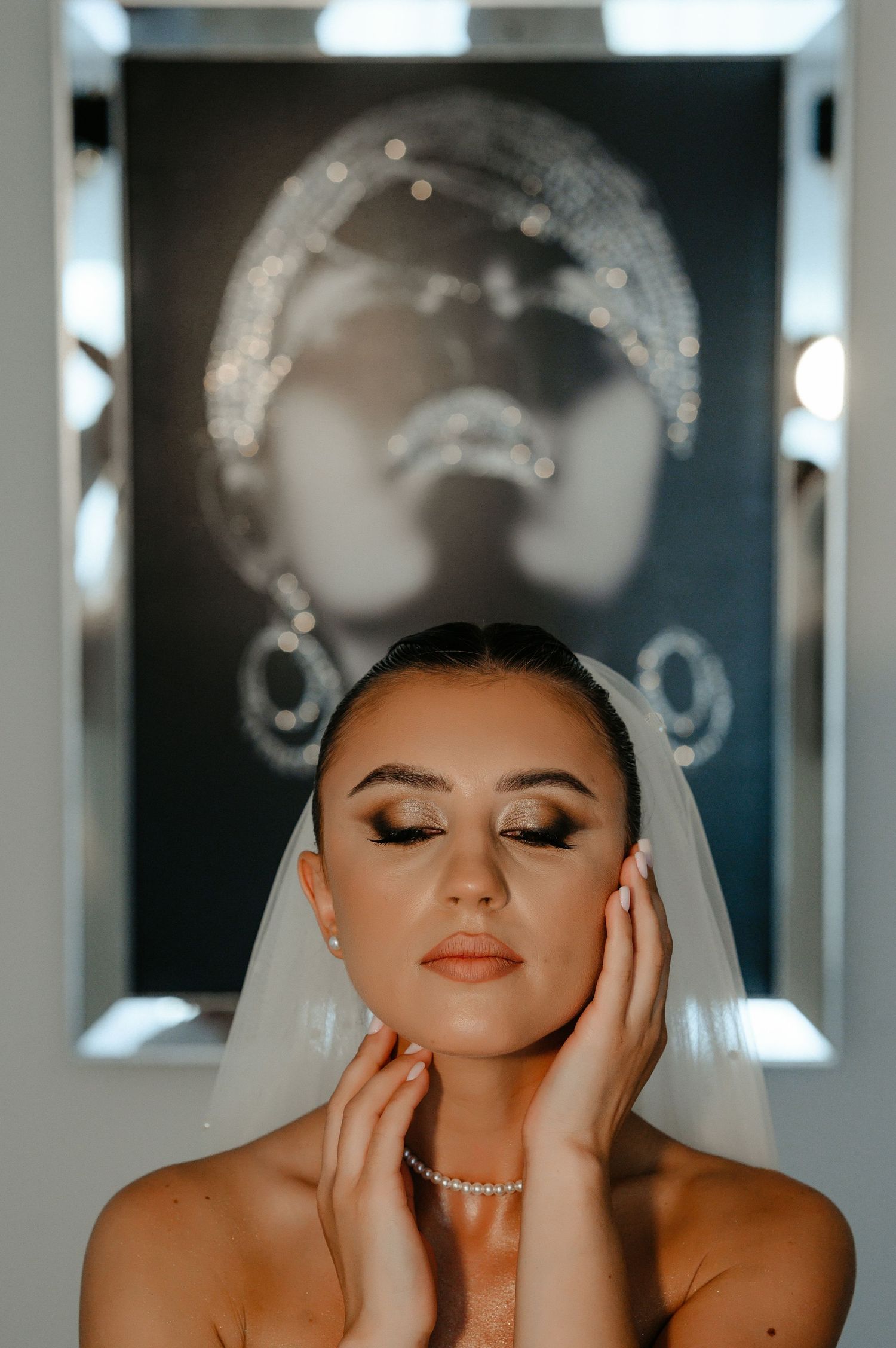 Close-up of bride with pearl necklace and veil posing before mirrored artwork.