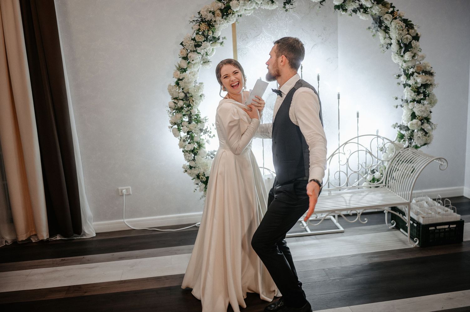 Bride and groom sharing first dance in front of a circular floral arch at wedding venue.