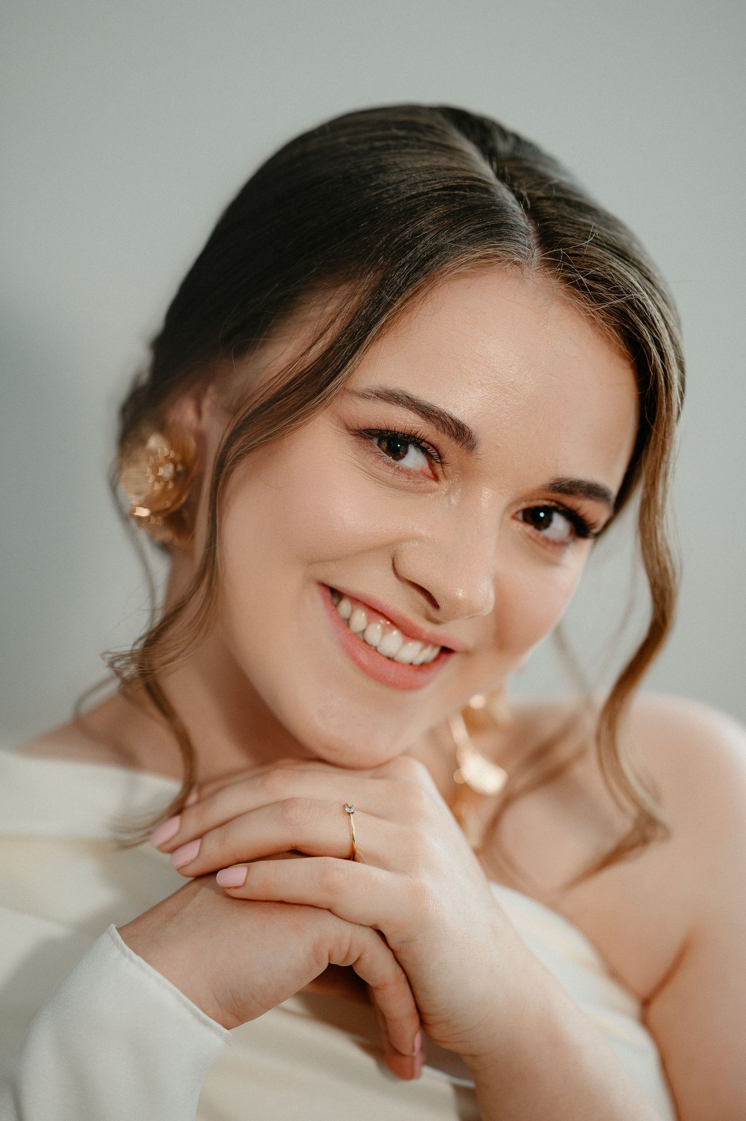 Beautiful smiling bride in a white dress with floral hair accessory and delicate gold jewelry.