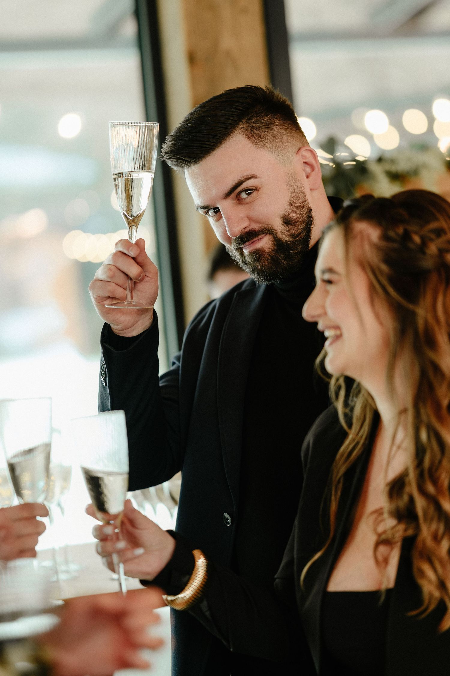 Bearded man in black suit raising a champagne flute in a toast at an elegant event.