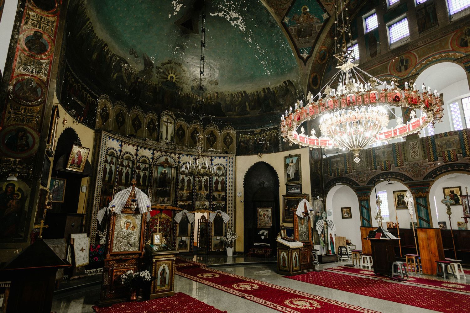Ornate Orthodox church interior with golden iconostasis, chandelier, and decorated domed ceiling.