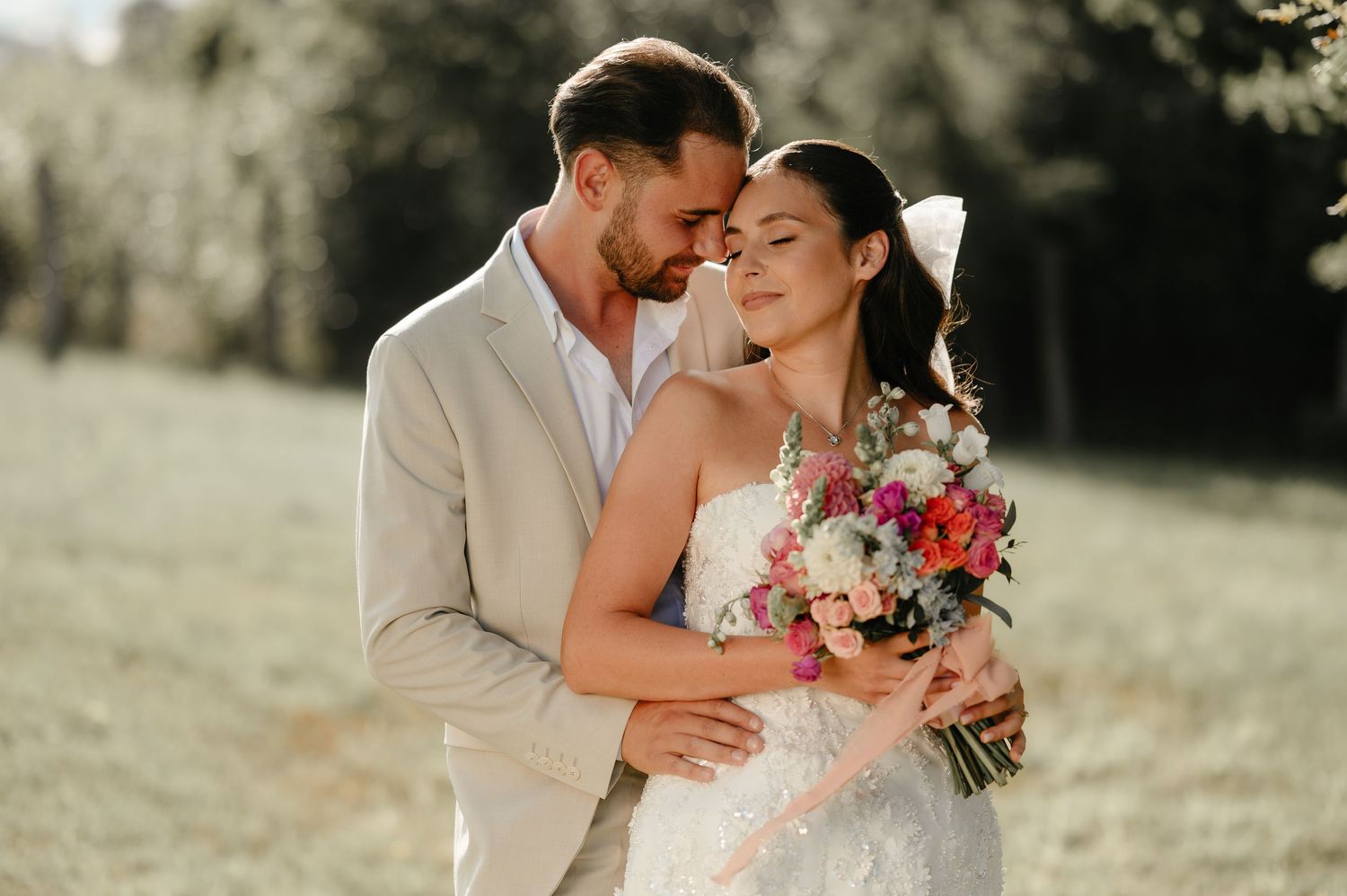Bride and groom sharing a tender moment outdoors, bride holding a vibrant floral bouquet.