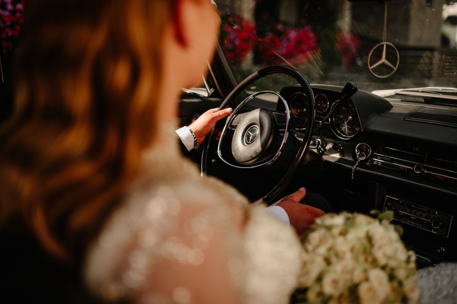 Bride holding bouquet near vintage Mercedes-Benz steering wheel.