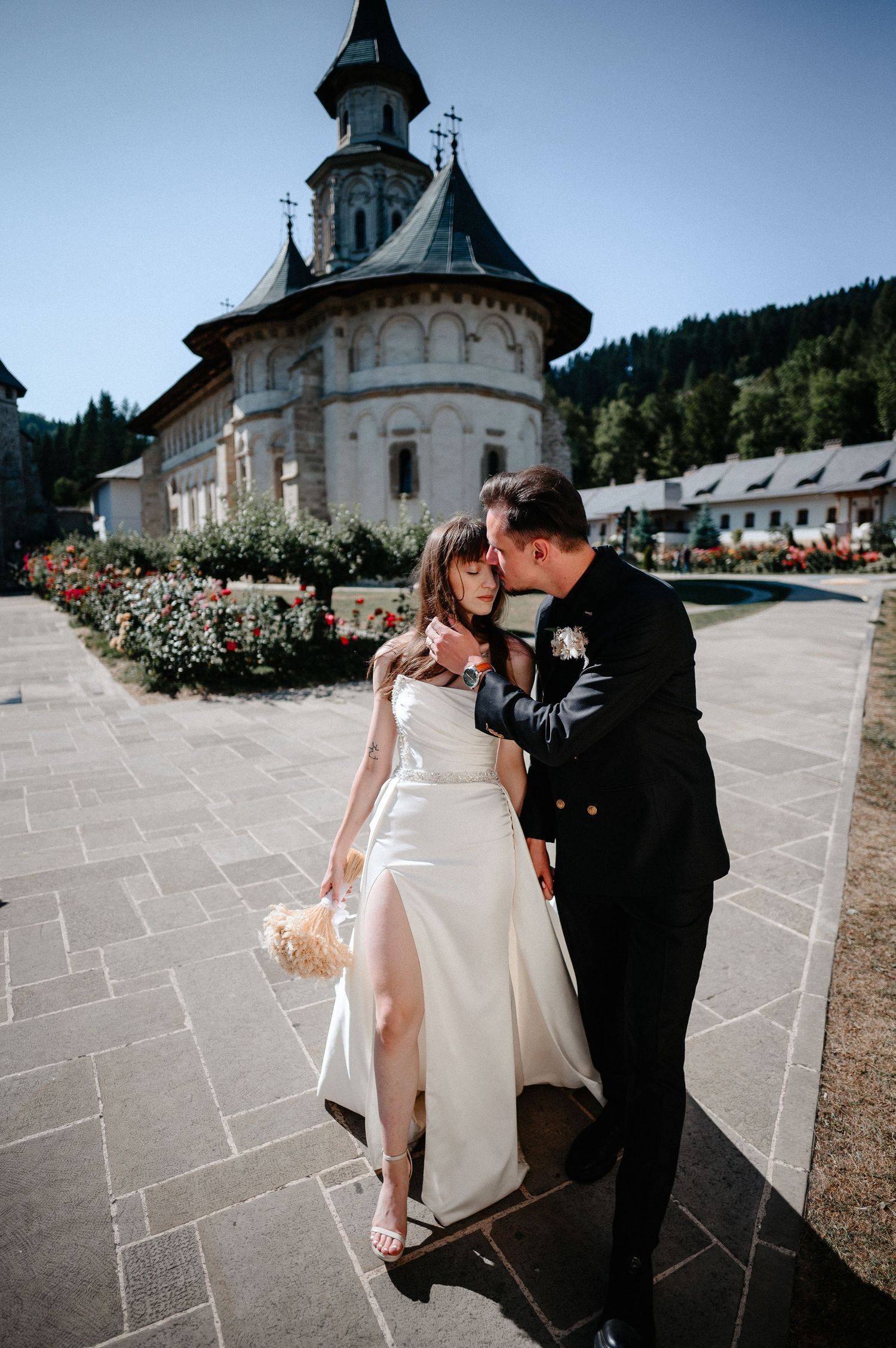 Bride and groom share romantic moment outside historic church with mountain backdrop on wedding day.