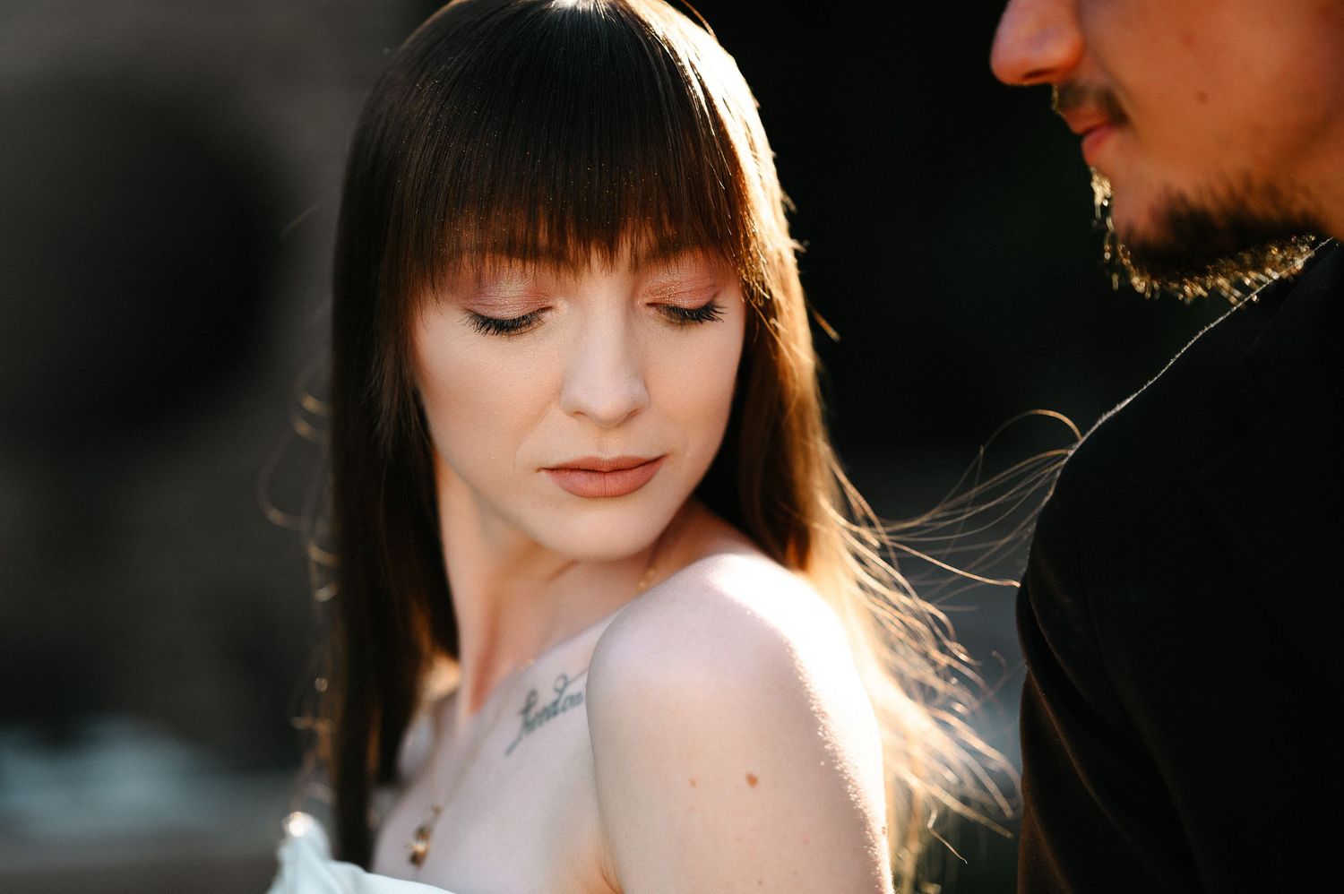 Close-up portrait of a bride with long bangs and a chest tattoo in soft natural sunlight.