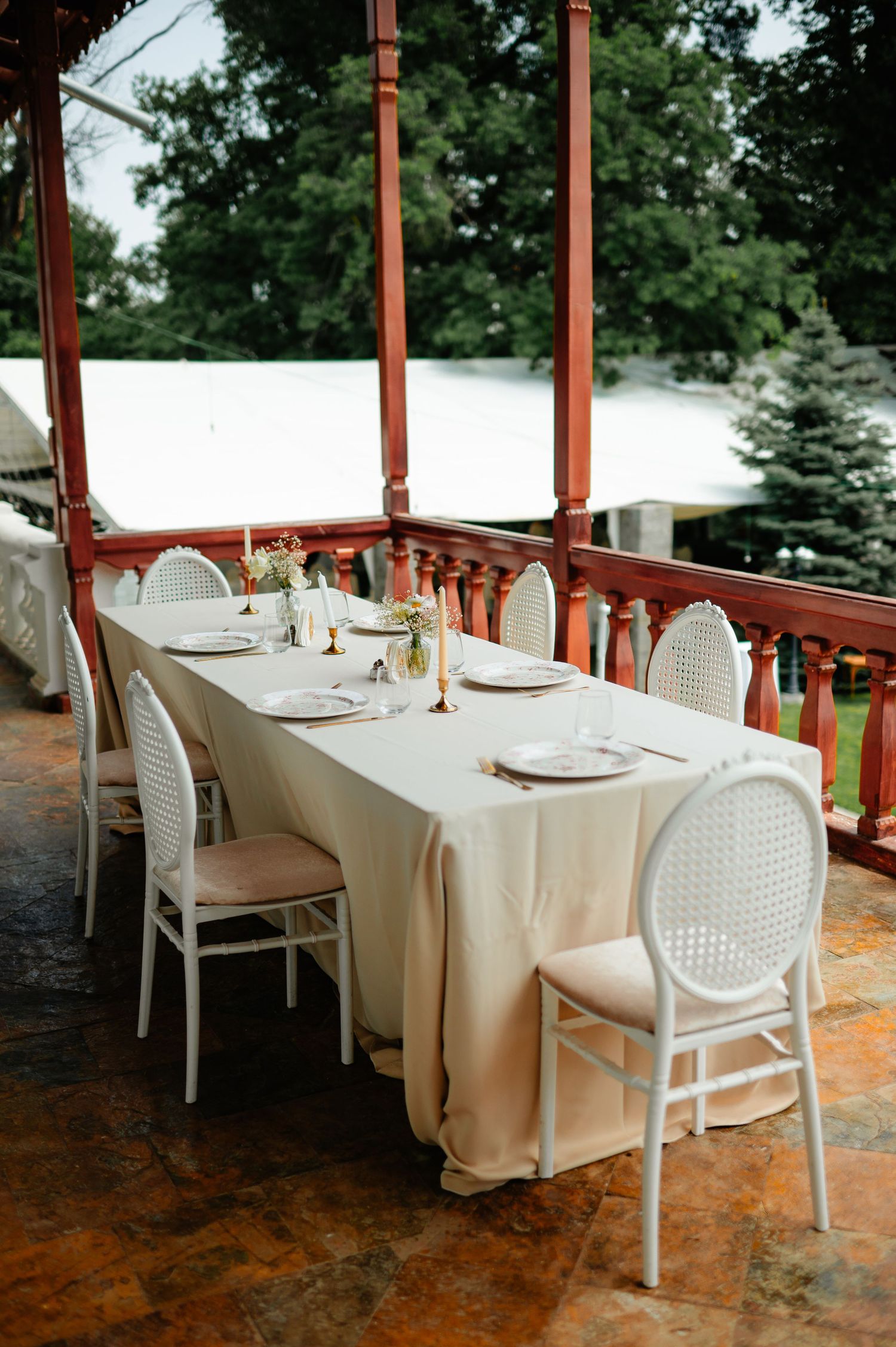 Elegant outdoor wedding reception table with white linen and chairs on a red wooden veranda.