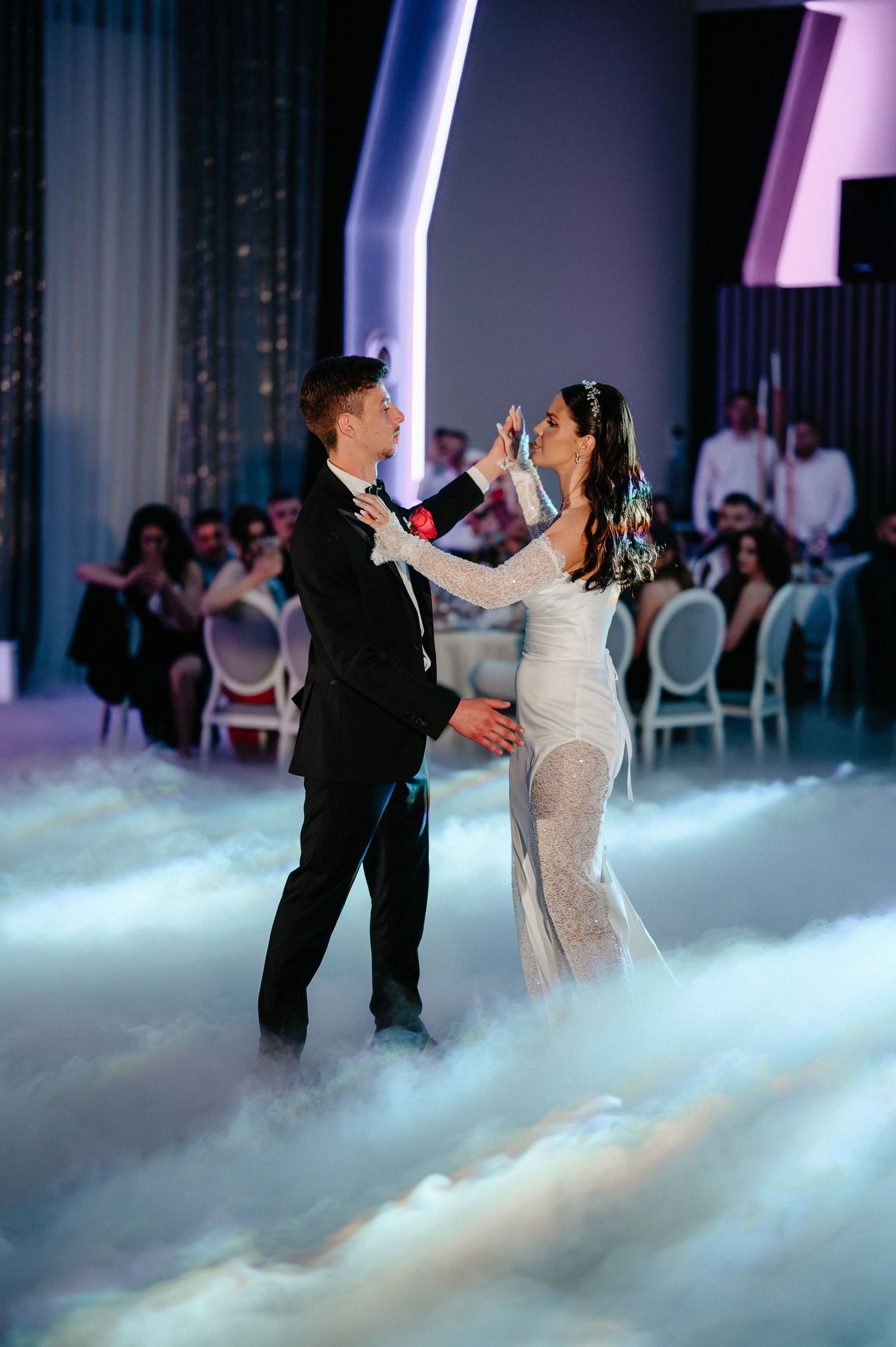 Newlyweds dance together on a cloud of fog at their elegant wedding reception with guests watching.