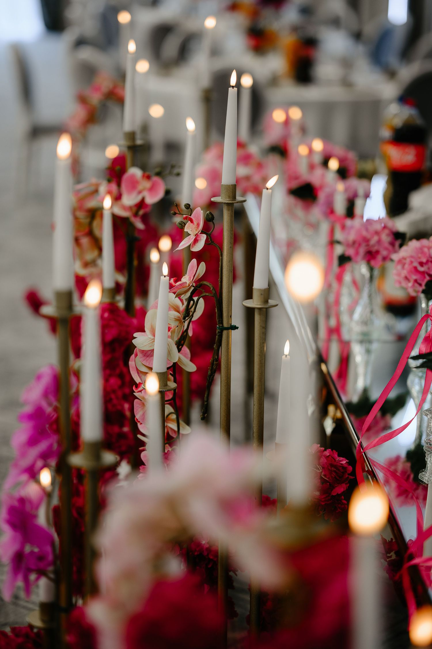 Close-up of wedding table with tall white candles, pink orchids, and fuchsia flowers.