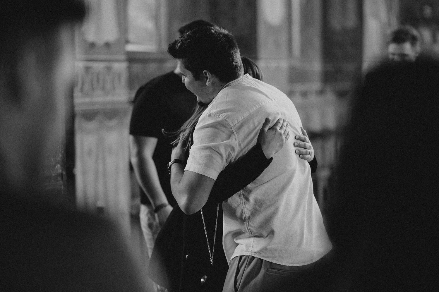 Two people share a warm embrace inside an ornate church in a black and white photo.