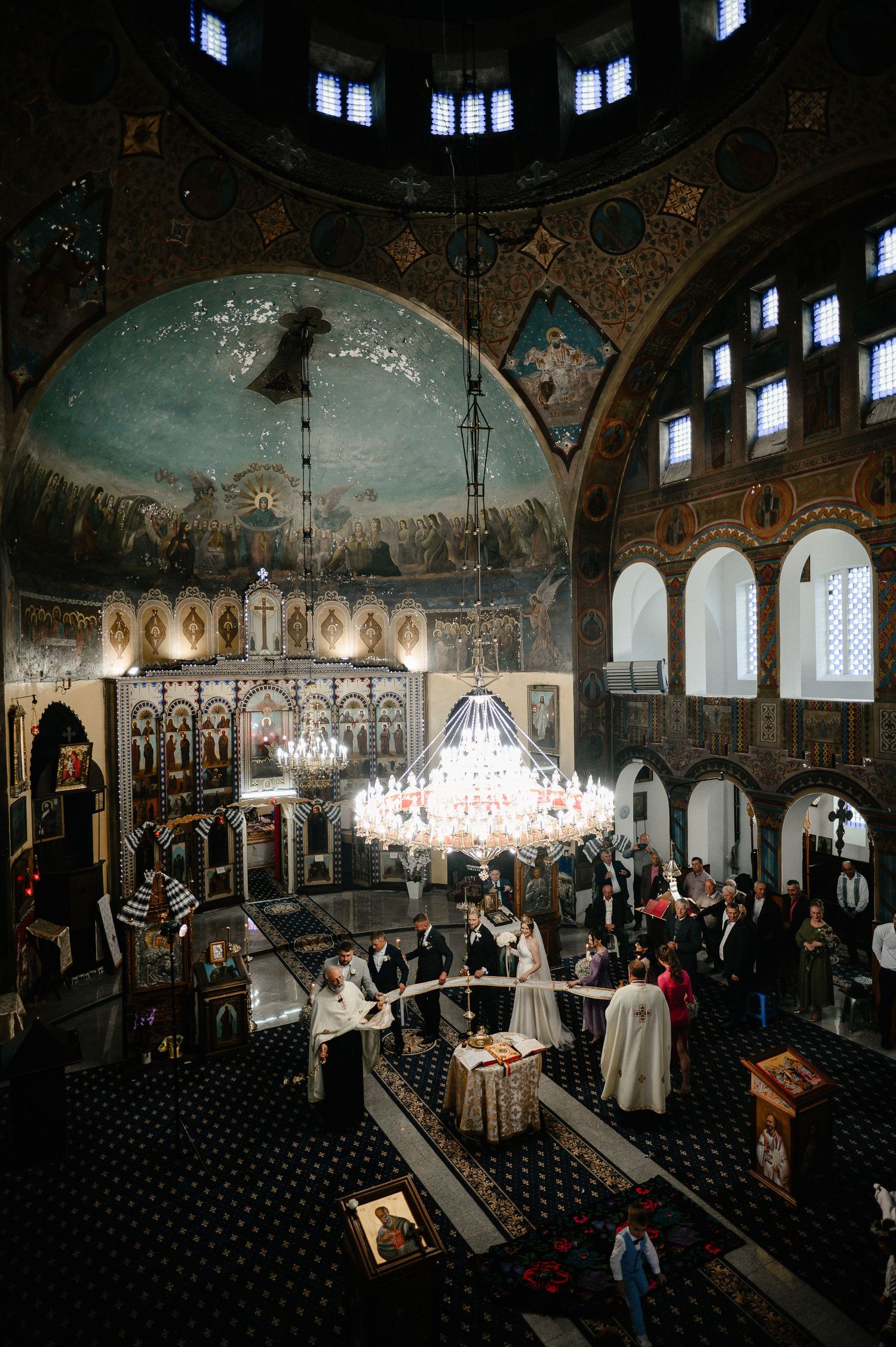 Wide angle view of Orthodox church wedding ceremony with ornate dome and chandelier.