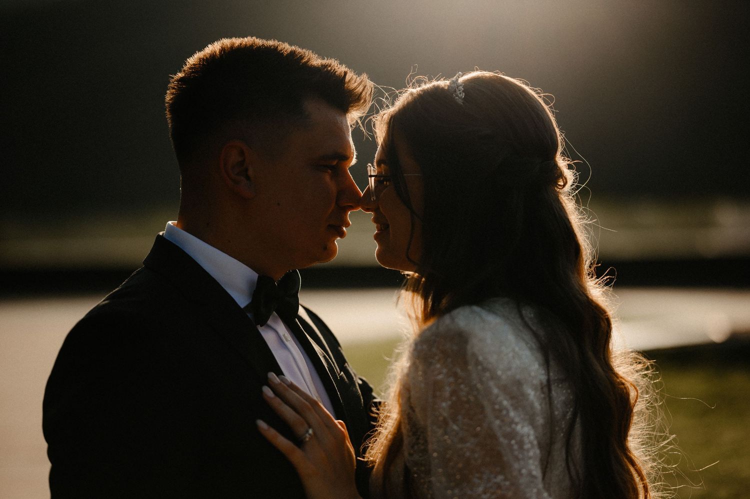 Romantic silhouette of bride and groom almost kissing in dramatic backlit outdoor setting.
