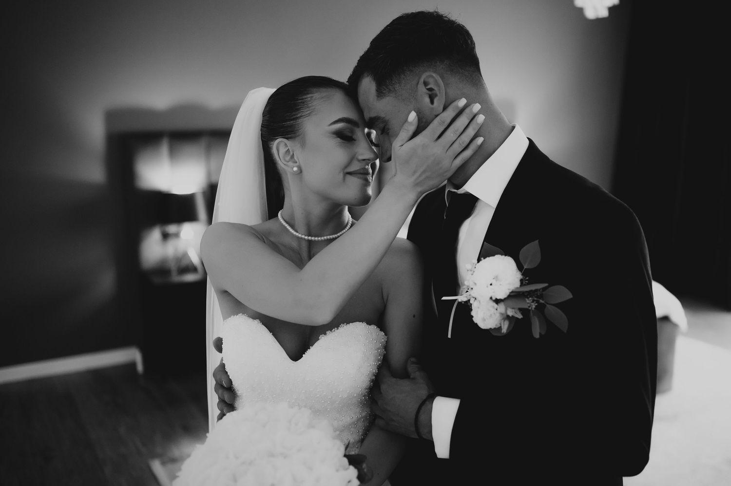 Romantic black and white portrait of bride and groom nearly kissing in soft moody lighting.