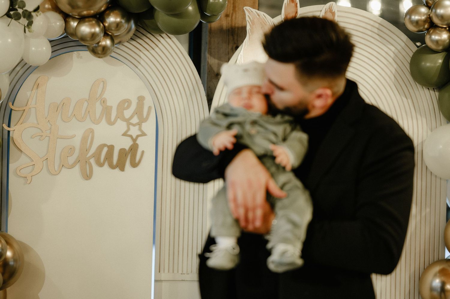 Father tenderly holding his newborn baby boy named Andrei Stefan at a woodland-themed christening celebration.