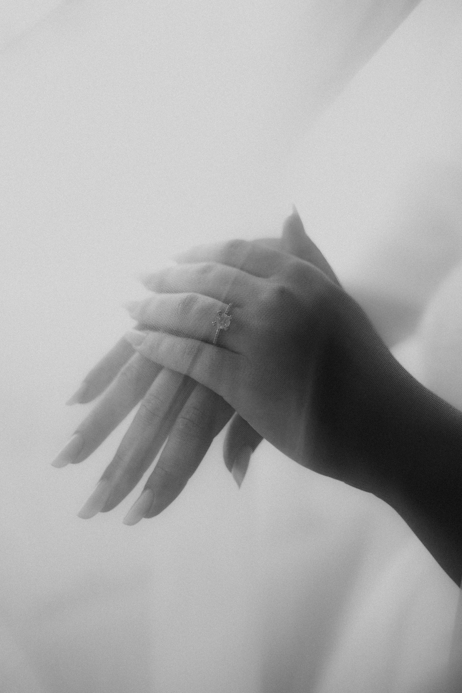 Black and white photo of elegant hands with a diamond engagement ring, soft dreamy background.